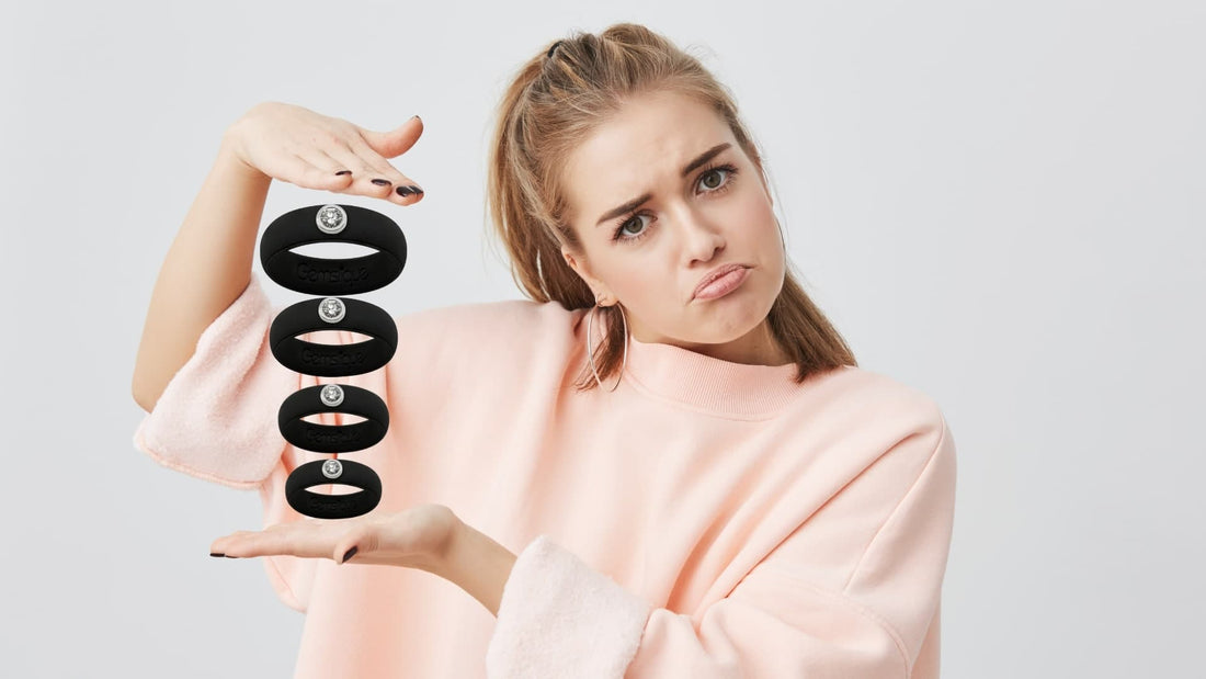 Young woman in a pink sweater holding and comparing stretched black Gemslique silicone rings with a puzzled facial expression.